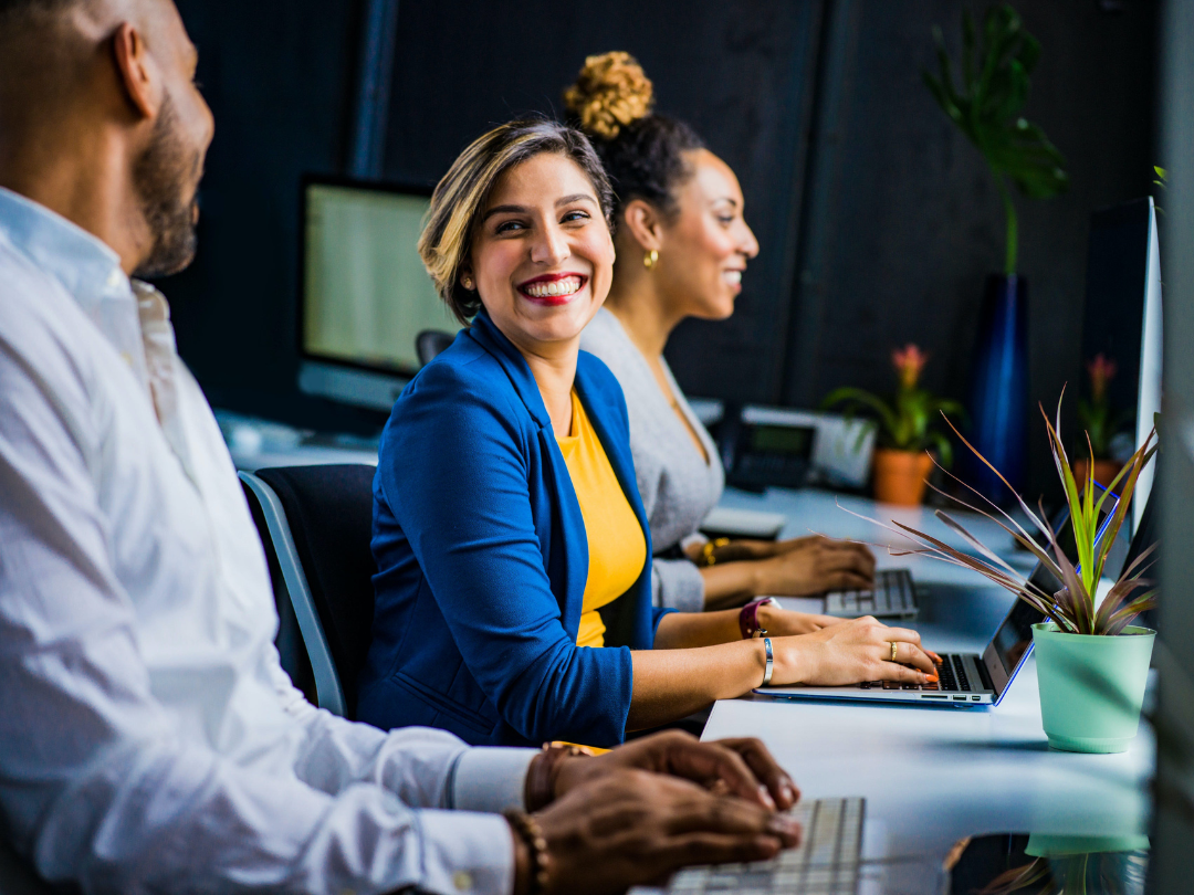 A diverse team of professionals sit working and talking at a desk