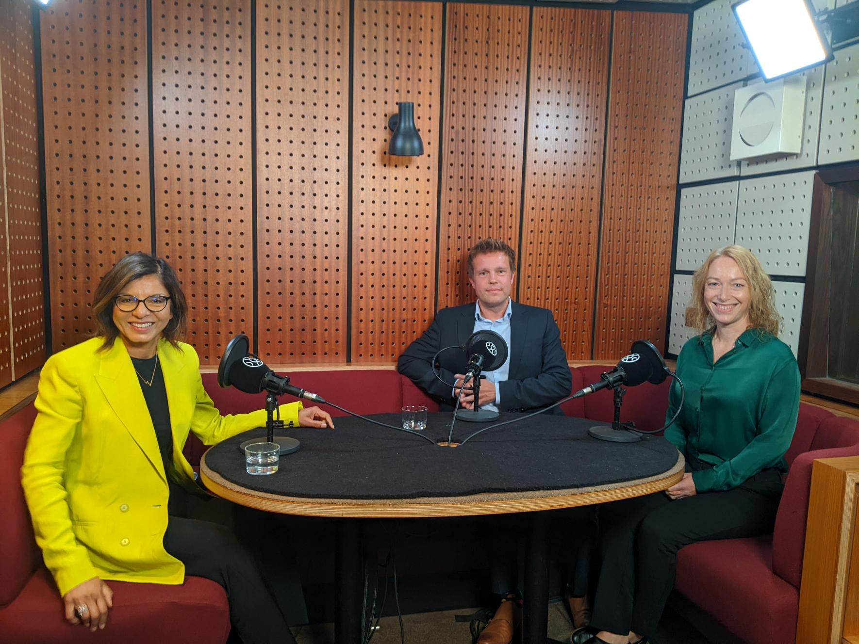 Three people sit smiling in a recording studio