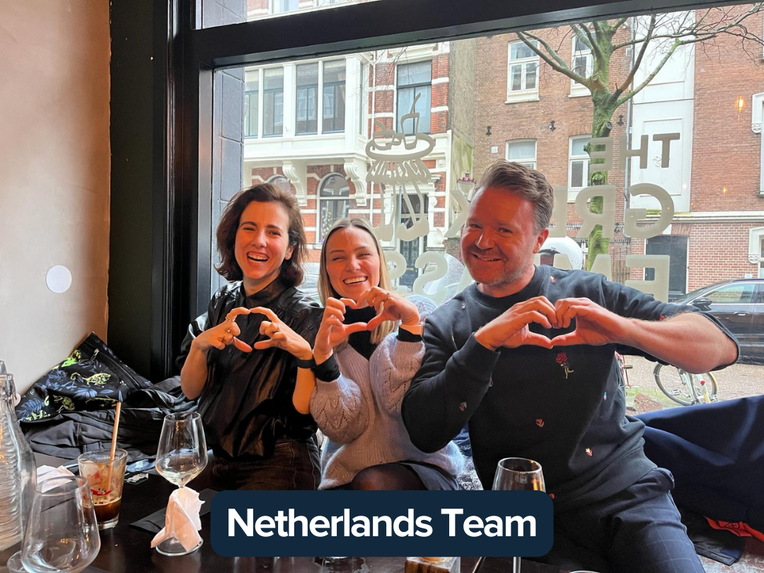 A group of people sit around a table making a heart with their hands and smiling