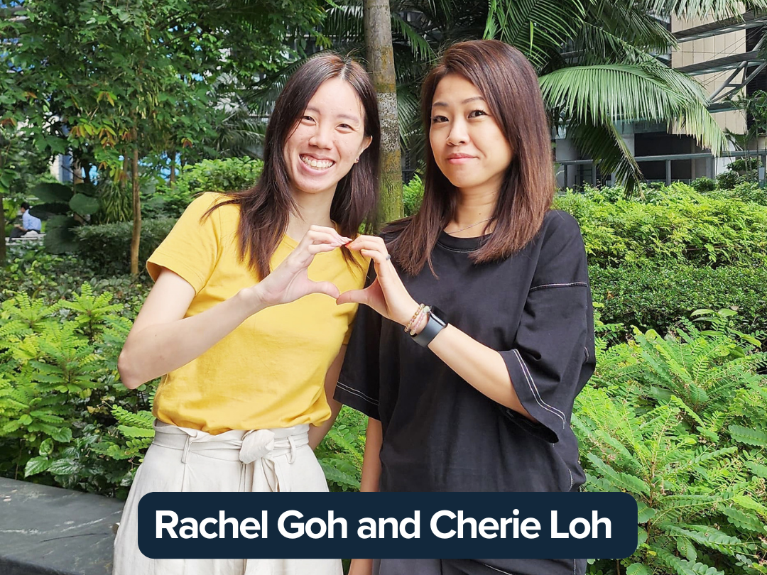 Rachel Goh and Cherie Loh stand together making a heart pose with their hands